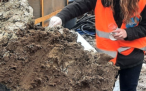 Tas de terre polluée avec une femme qui prélève un échantillon pour faire des analyses sites et sols pollués